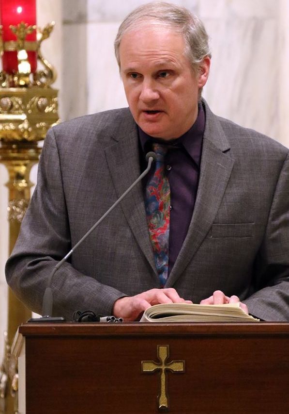 Bill lectoring from the altar dressed in a suit