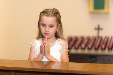 Haylee, a young blind girl with blonde hair, pictured kneeling in her church on her First Communion Day