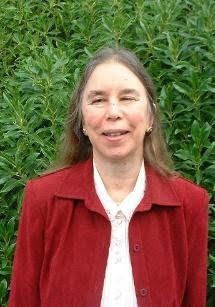 Lynn in front of some foliage smiling in a red coat 