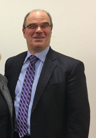 Dick pictured at our offices in New York smiling wearing a suit and glasses