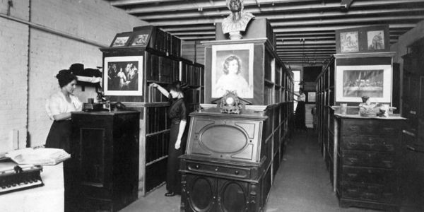 A historic image of our library showing stacks of books and two women working