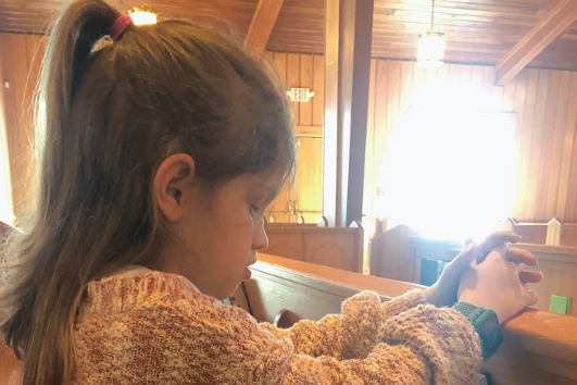A young blind girl praying in her church