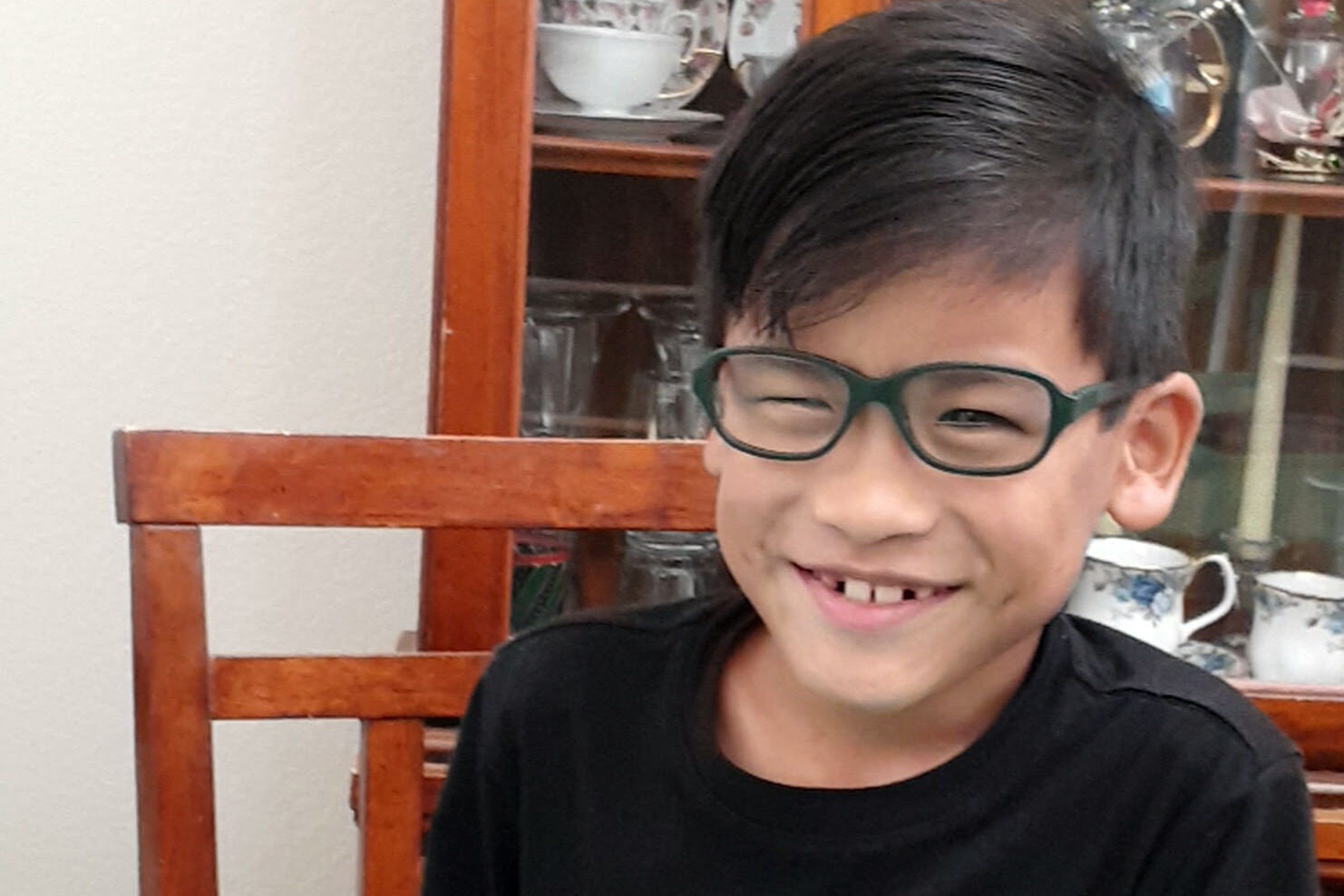 Levi, a young boy, wearing green glasses and a black T-shirt, smiling cheekily for the camera. 